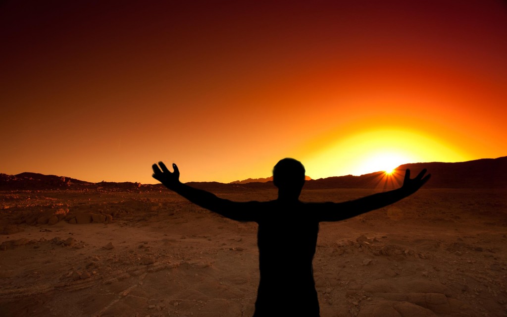 Man with out stretched hands toward the rising sun in the desert